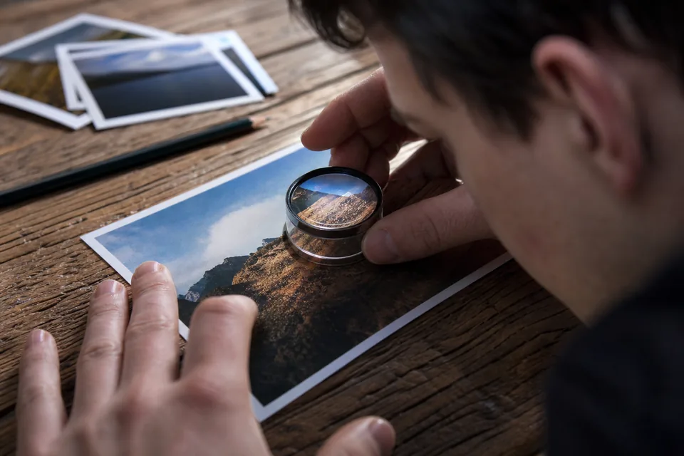 Glass loupe resting on a printed photo on an oak table, showing fine detail of the print