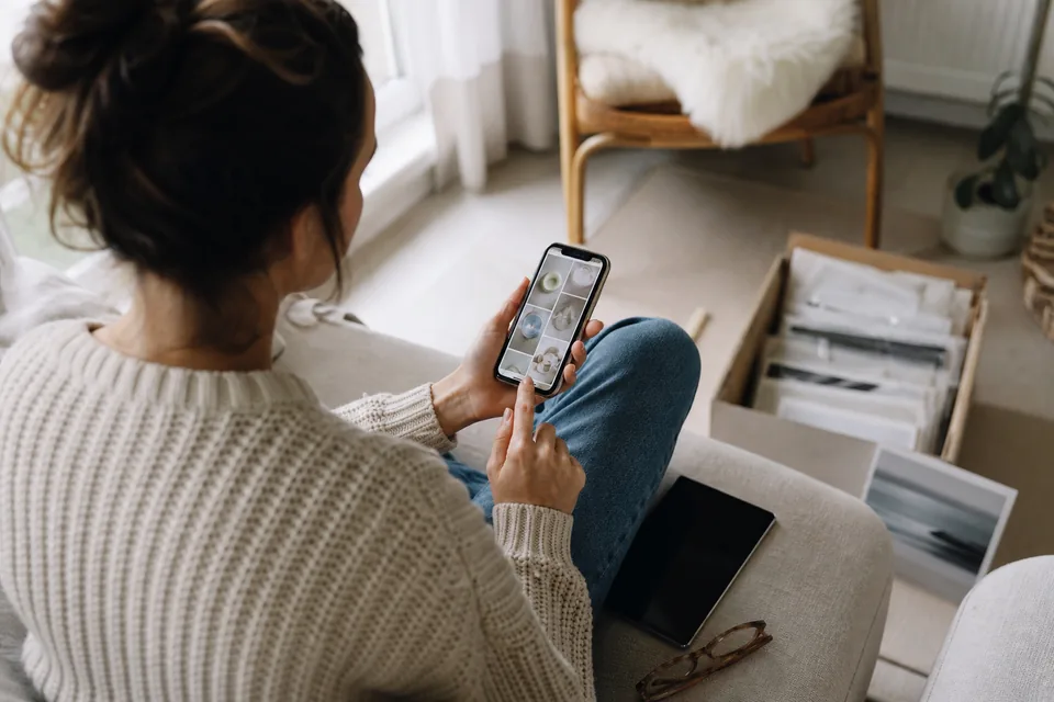 Adult on a sofa holding a phone and looking through family photos, a tablet on the cushion beside